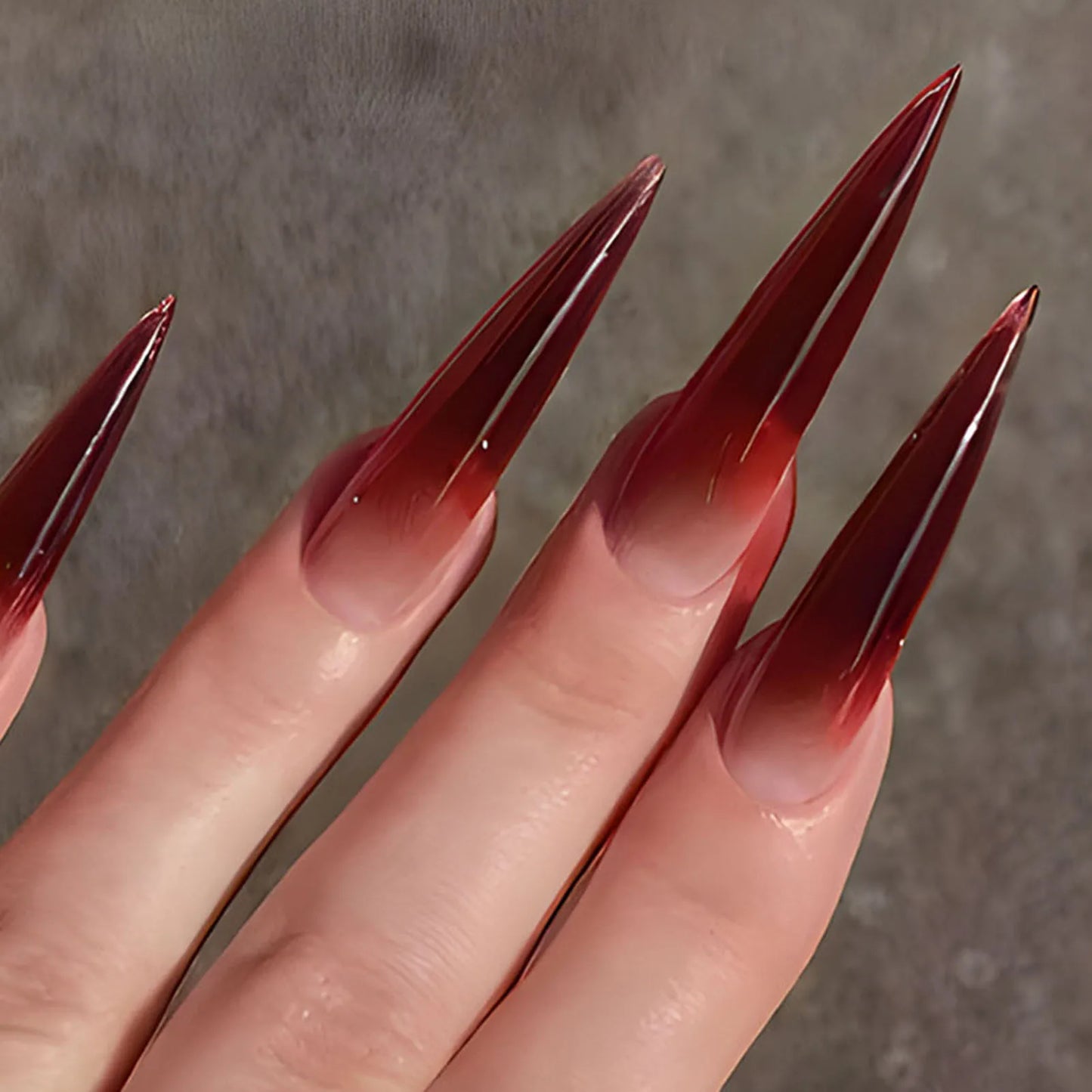 Hand with long stiletto-shaped ombre red press-on nails, showcasing nail art tiers