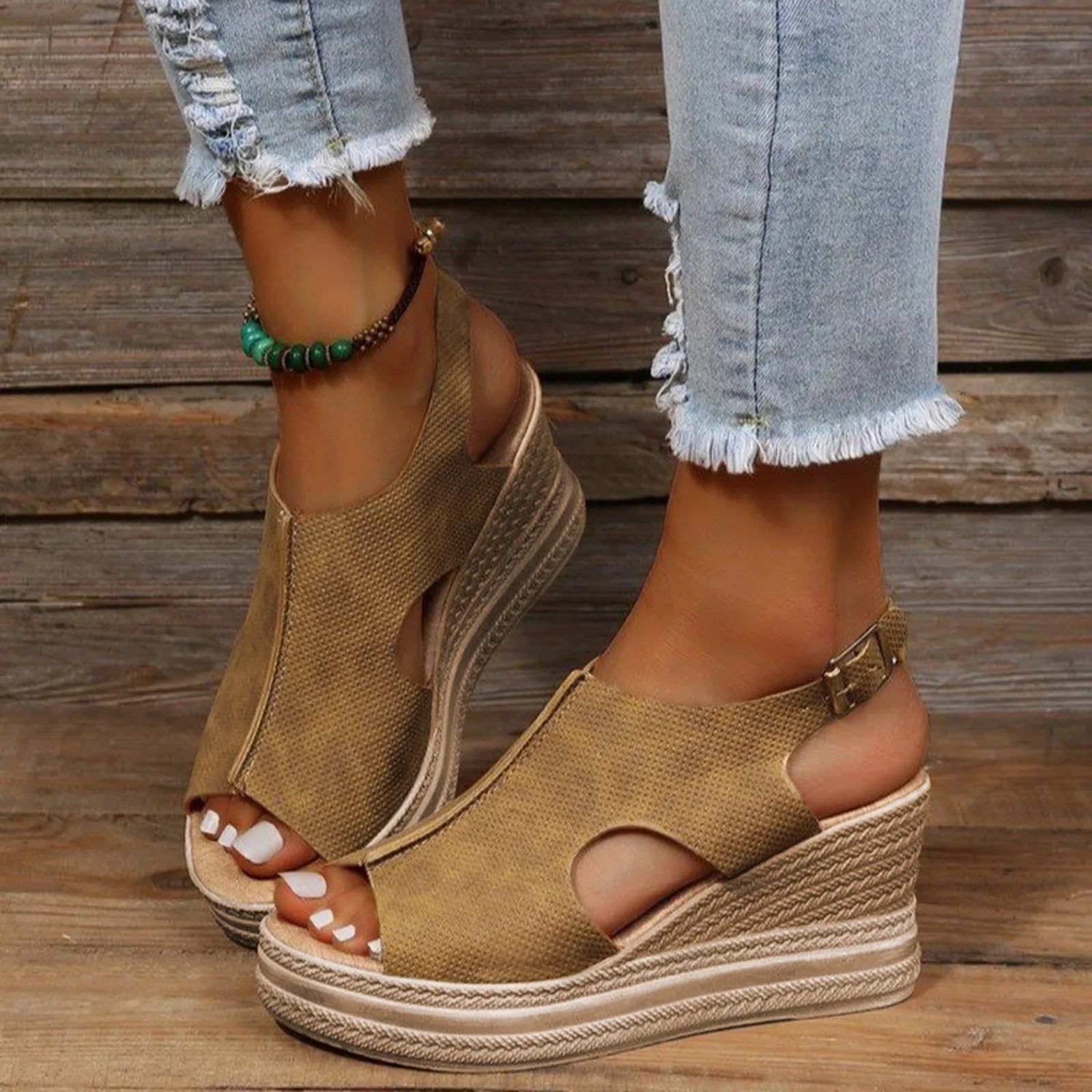 Women’s tan wedge sandals with cutout details, paired with frayed hem jeans, wood background