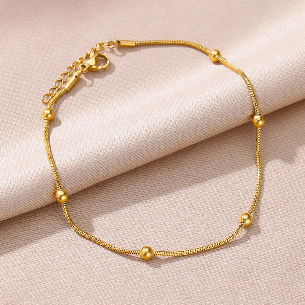 Gold adjustable bracelet with delicate round beads on a soft beige fabric background