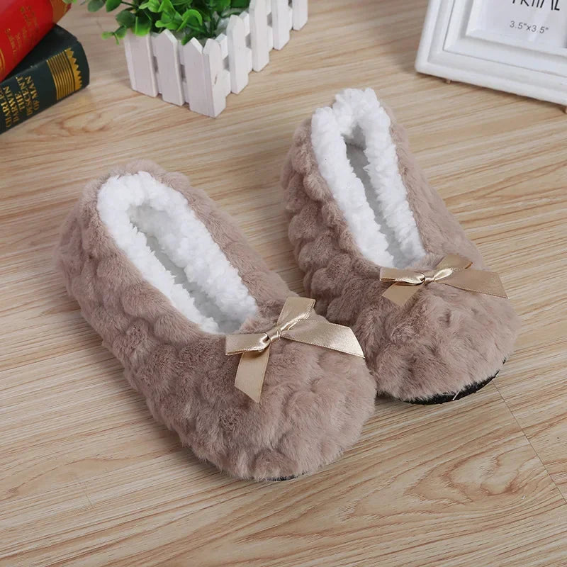 Plush beige slippers with white fleece lining and satin bows on a wooden floor, cozy loungewear.