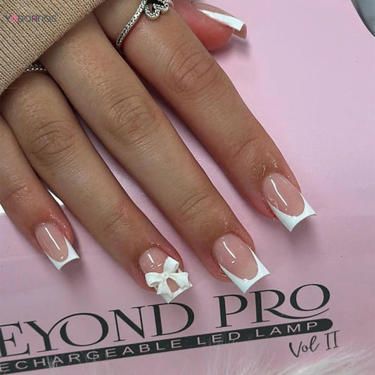 Hand displaying French tip coffin nails with 3D white bow accent for concierge tier showcase