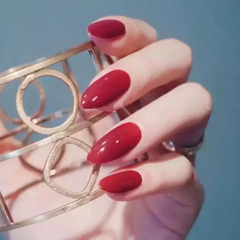 Hand with glossy red almond nails holding a gold geometric bangle, showing Concierge Tiers